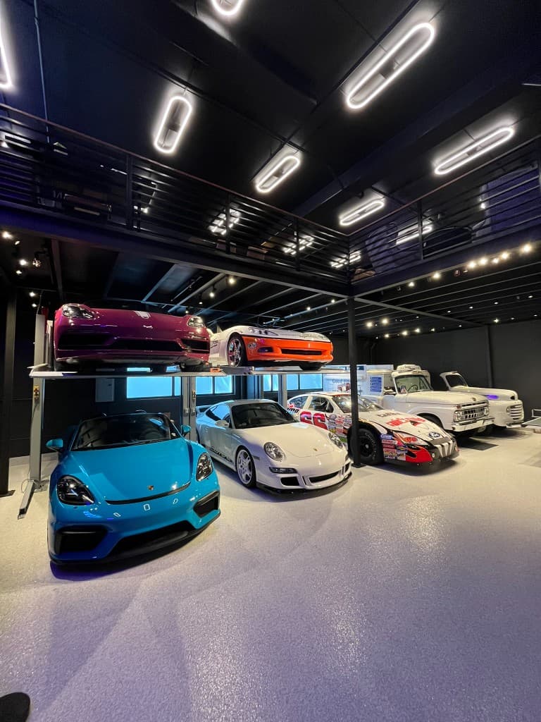 Collector garage showroom with sports cars on the floor and stacked on lifts under oval LED ceiling lights
