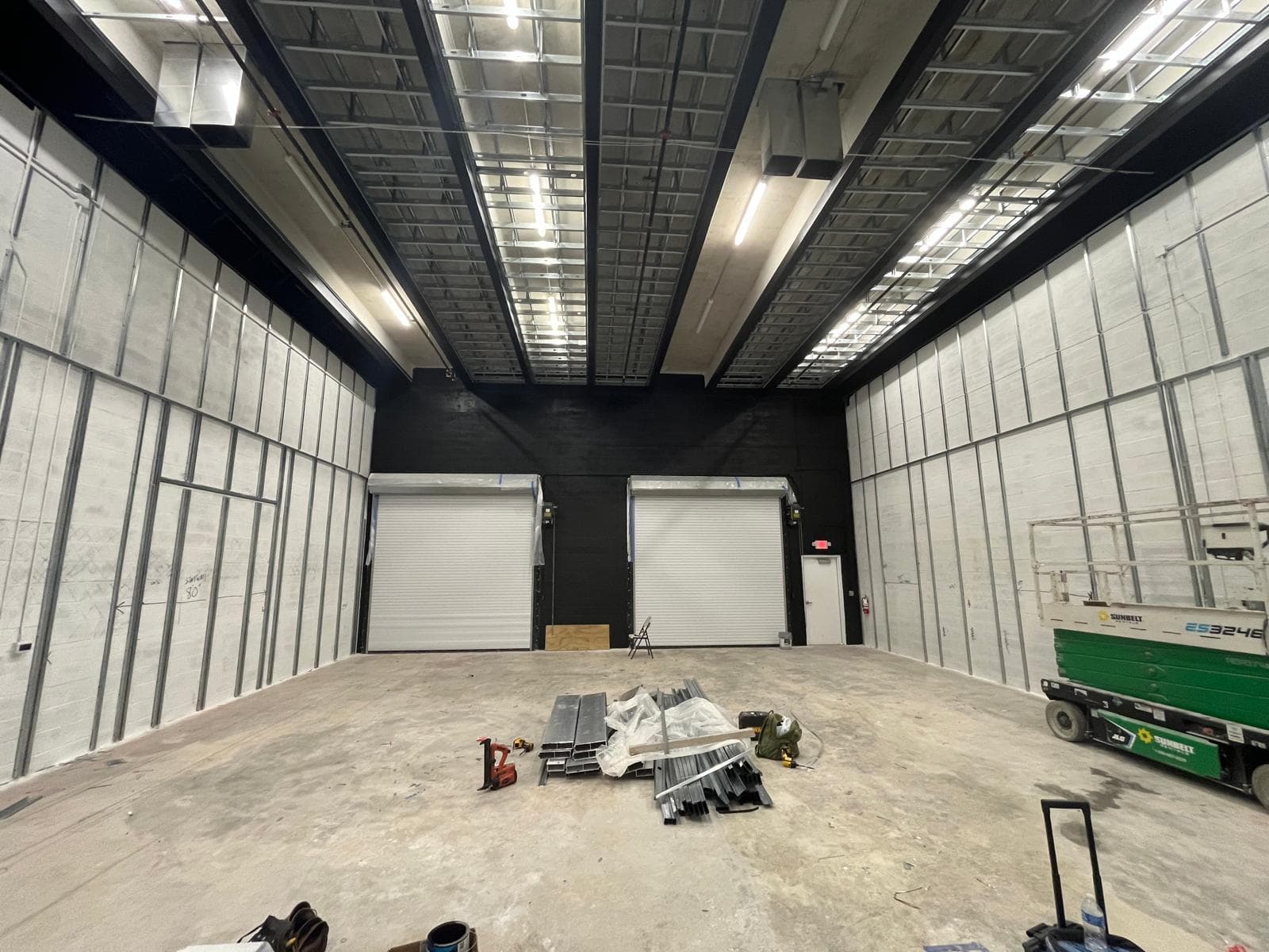 Commercial bay shell with white corrugated wall panels, black steel ceiling structure and two white roll-up doors