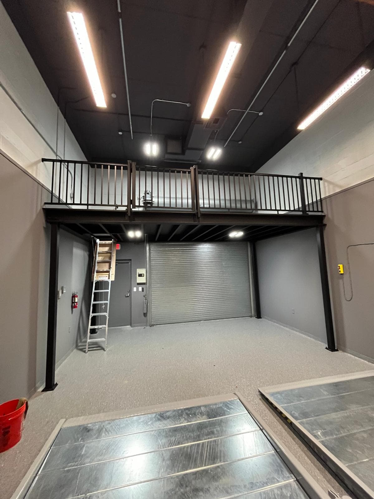 Finished garage bay with a black steel mezzanine, roll-up door and light speckled epoxy floor