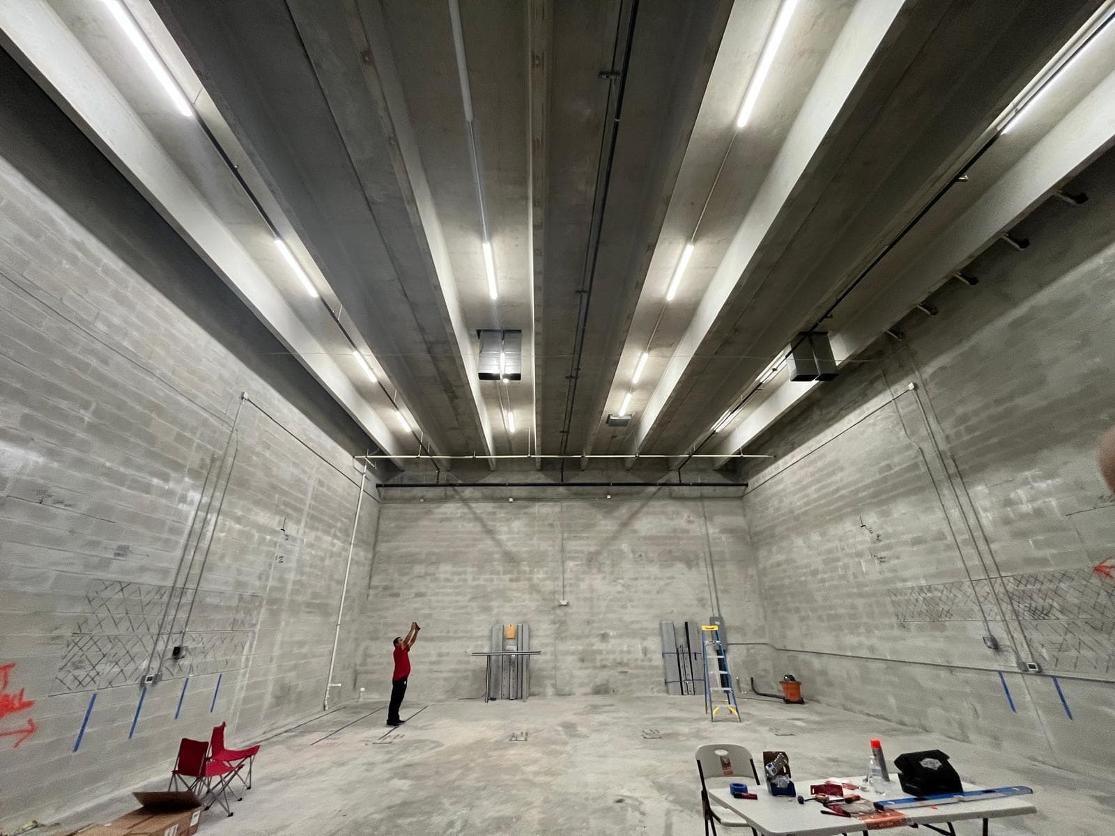 Very tall concrete industrial hall with rows of linear lighting and a worker at the wall for scale