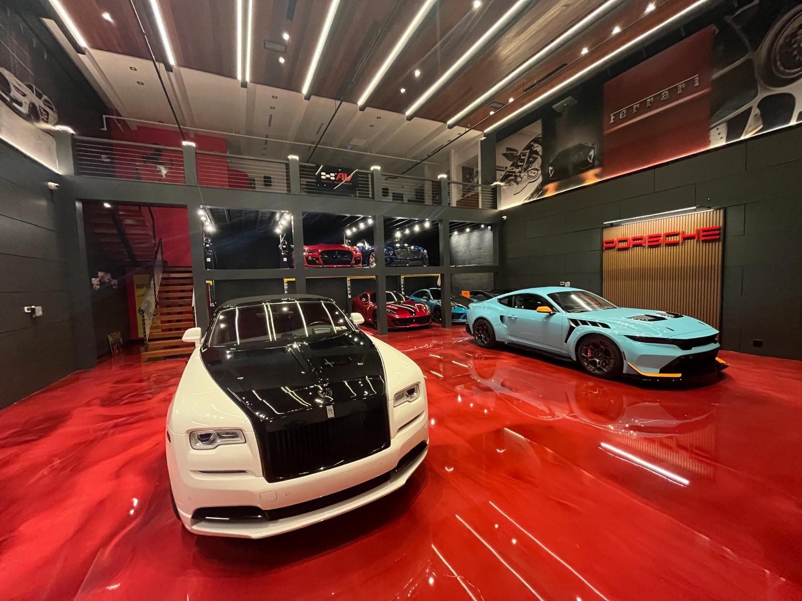 Two-level exotic car gallery with high-gloss red epoxy floor, sports cars on display and a mezzanine of glass display bays