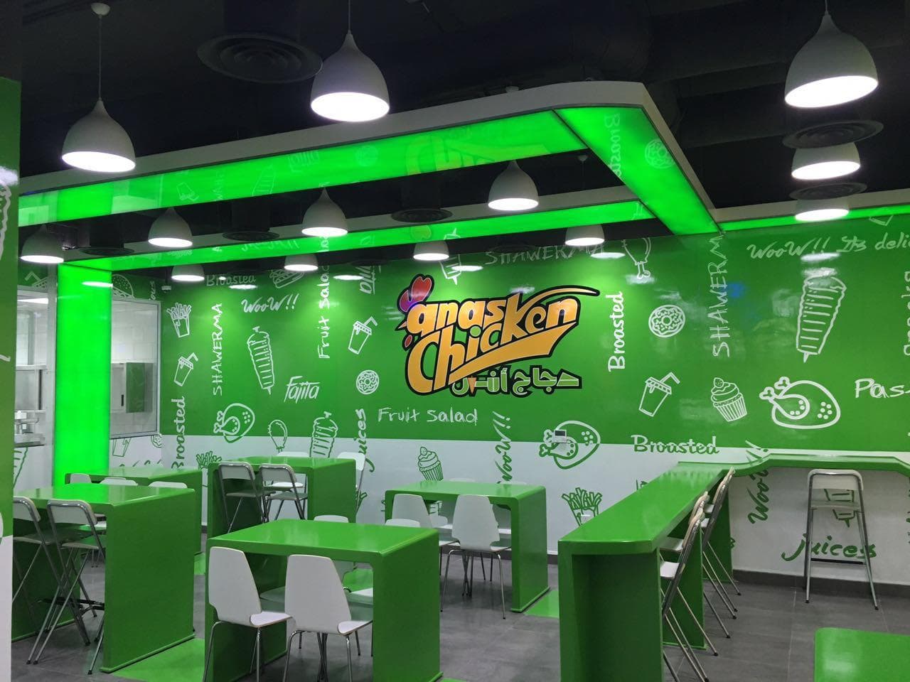 Finished fast-casual restaurant dining room with green branded wall graphics, green tables and a backlit green ceiling feature